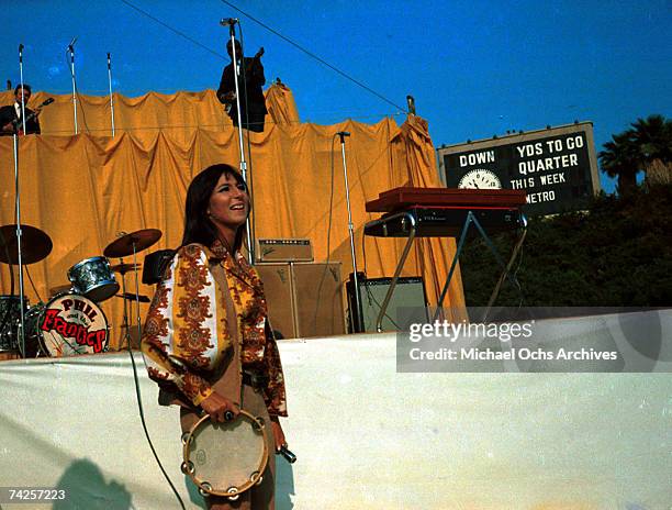 Entertainer Cher performs onstage holding a tambourine in front of a riser that has a drum kit with the logo for the band "Phil And The Frantics" on...