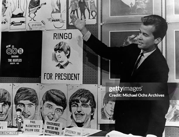 Television show "American Bandstand" host Dick Clark stands in fron of some "Beatles" paraphernalia including a "Ringo For President" poster, a sign...