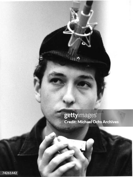 Bob Dylan wearing a motorcycle hat playing harmonica into a microphone in Columbia Recording Studio for a session in September 1961 in New York City,...
