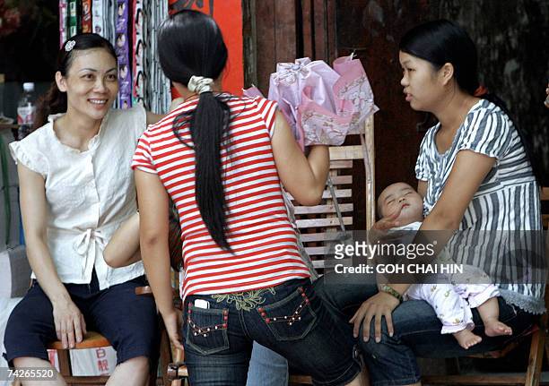 Young Chinese mother holds on to her baby as she chats with her friends outside a shop in Bobai town, southern China's Guangxi region 24 May 2007....