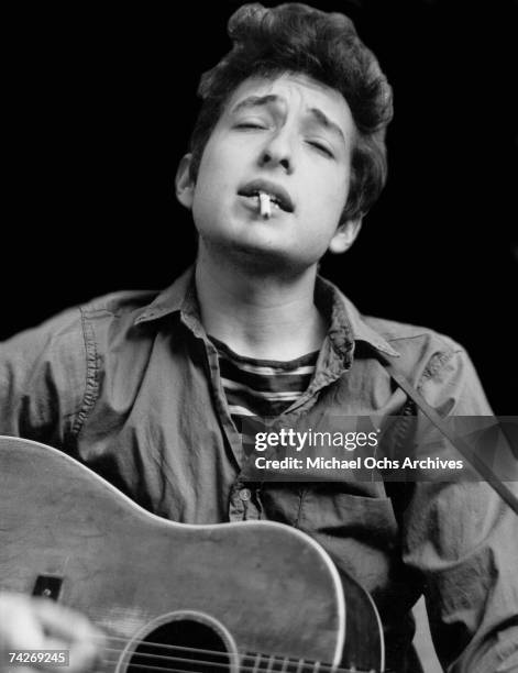 Bob Dylan plays acoustic guitar and smokes a cigarette in this headshot from September 1962 in New York City, New York.