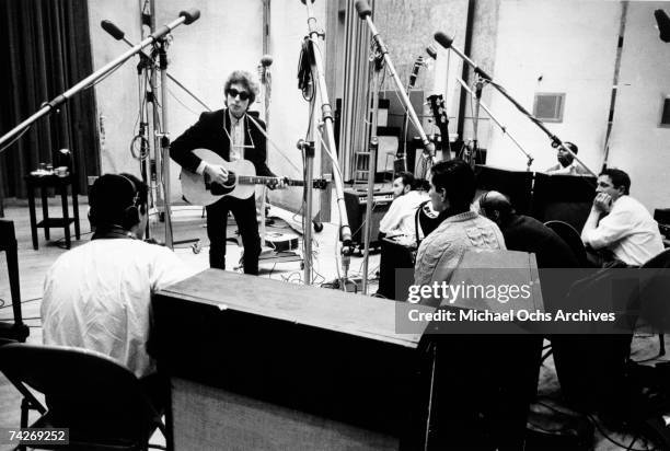 Bob Dylan strums a Gibson acoustic guitar with a harmonica around his neck and wearing Ray-Ban sunglasses with session guitar player Kenny Rankin in...