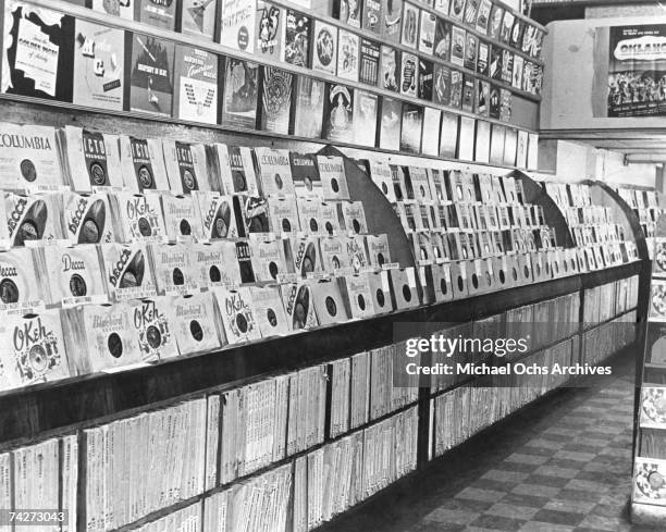 An interior view of a record store from the 1950's which shows albums with various record company labels including Columbia, Decca, Okeh, and...