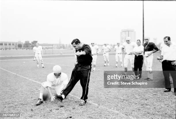 View of University of Notre Dame football coach Ara Parseghian as he demonstrates kicking form during practice on the field, South Bend, Indiana,...