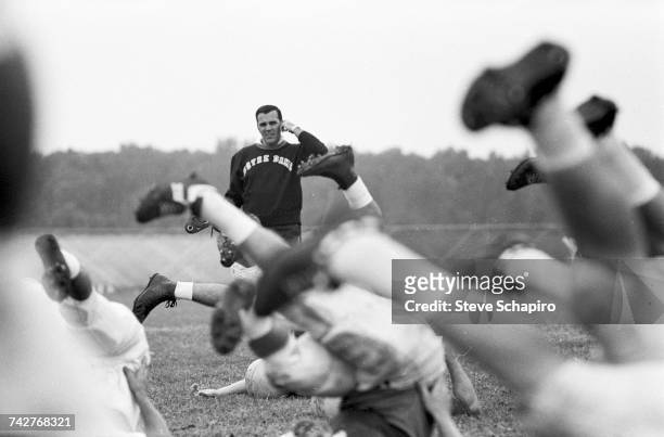 View of University of Notre Dame football coach Ara Parseghian as he oversees a players' stretching session on the field, South Bend, Indiana, 1964.