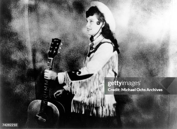 Loretta Lynn wears a cowboy hat and a fringe western style jacket while holding an acoustic guitar as she poses for a portrait in circa 1960 in...