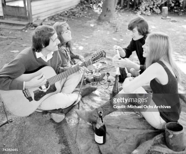 Denny Doherty, Michelle Phillips, John Phillips and Mama Cass Elliott have an acoustic guitar jam and picnic in circa 1966 in a park.
