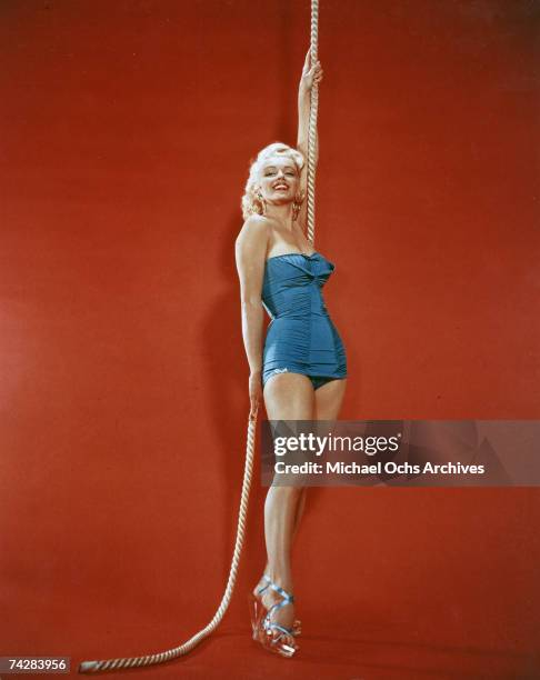 Actress Marilyn Monroe poses for a portrait holding on to a rope wearing a blue bathing suit and glass high heels in circa 1952.