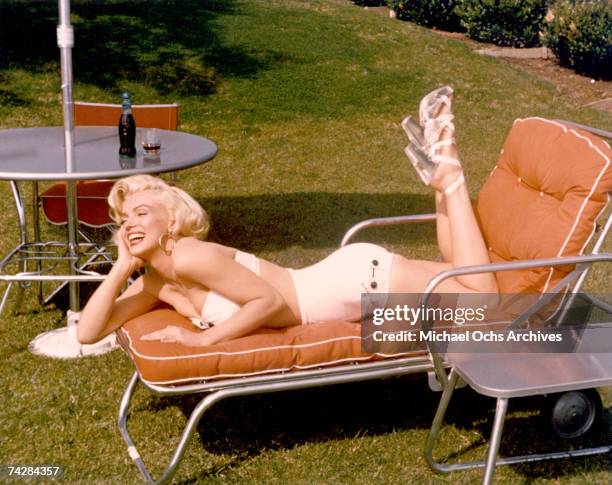 Actress Marilyn Monroe poses for a portrait in a bathing suit and high heels with a bottle of Coca-Cola in a glass on a table behind her in circa...