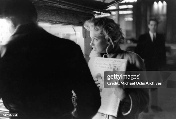 Actress Marilyn Monroe picks up a copy of the New York Dail Post newspaper at a newstand in March 1955 in New York City, New York.