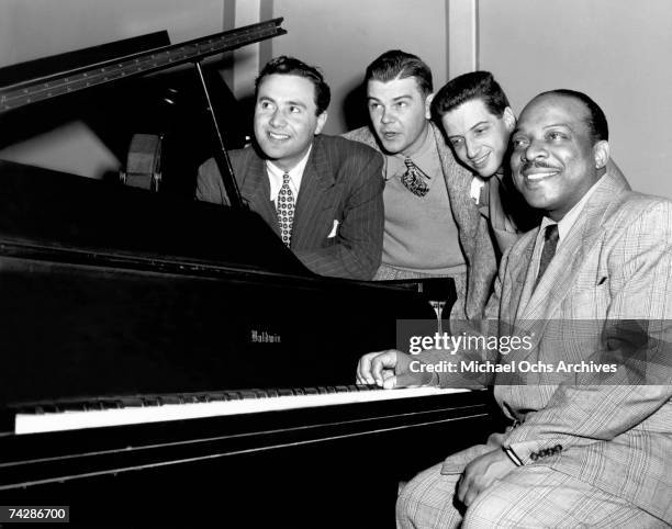 Big Band leader Count Basie sits at the Piano accompanied by DJ and record company owner Gene Norman an unidentified man and producer John Hammond on...