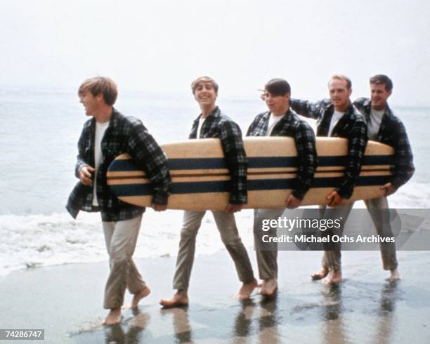 Rock and roll band "The Beach Boys" walk along the beach holding a surfboard for a portrait session in August 1962 in Los Angeles, California. Dennis...