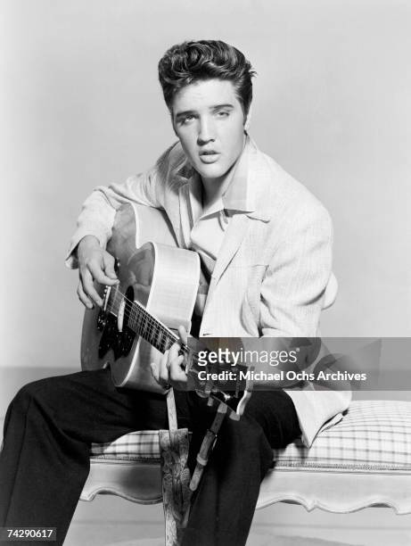 Rock and roll singer Elvis Presley strums his acoustic guitar in a portrait in 1956.