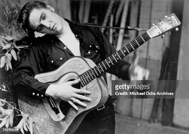 Rock and roll singer Elvis Presley poses for a portrait holding an acoustic guitar in 1956.