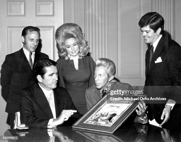 Country singer Porter Wagoner flanked by Dolly Parton and two other men presents a man with an "Honorary Wagonmaster" plaque in circa 1968.