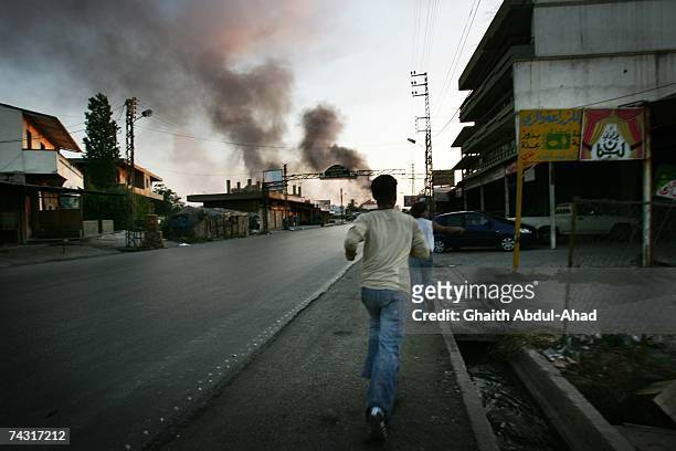 Men run away from sniper fire as smoke rises in the distance from the Palestinian refugee camp Nahr al-Bared, where the Lebanese army is fighting the...