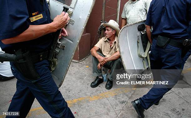 Tegucigalpa, HONDURAS: Policias antidisturbios pasan frente a un campesino que permanece sentado durante una protesta frente al Ministerio Publico,...