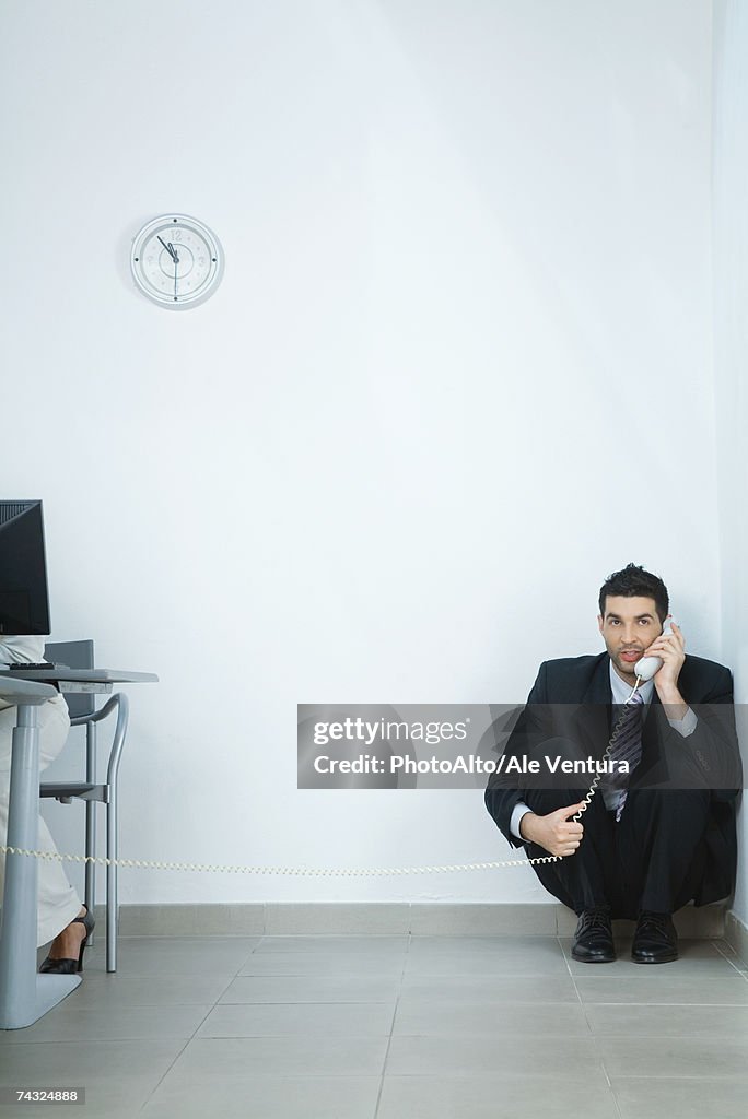 Businessman sitting on floor, in corner, talking on phone