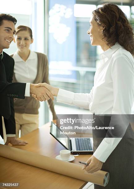 mature female architect shaking hands with young male client - customer profile stock pictures, royalty-free photos & images