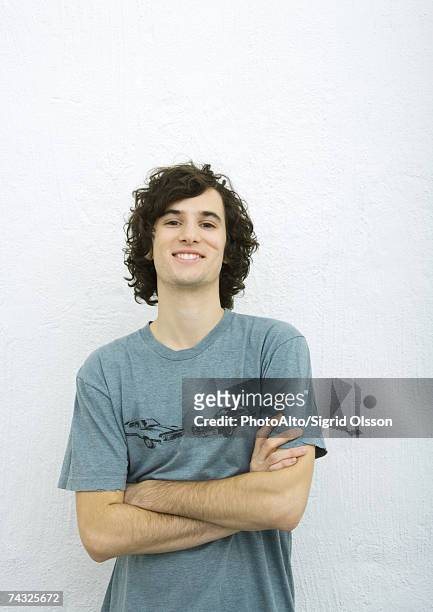 young man with arms crossed, smiling at camera, portrait, white background - ventenne foto e immagini stock