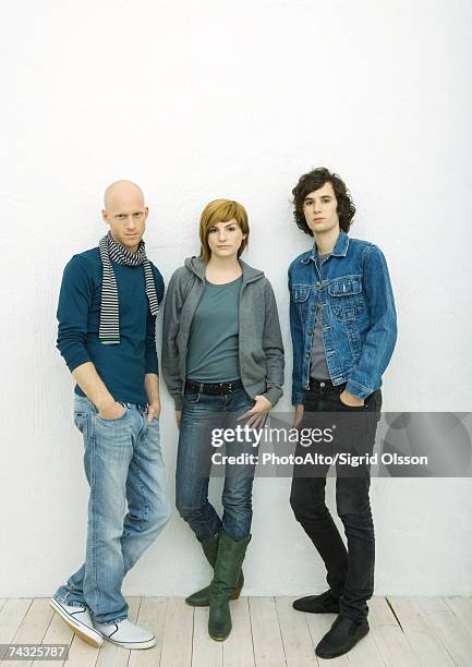 three young adults leaning against wall, looking at camera, full length portrait, white background - three people isolated stock pictures, royalty-free photos & images