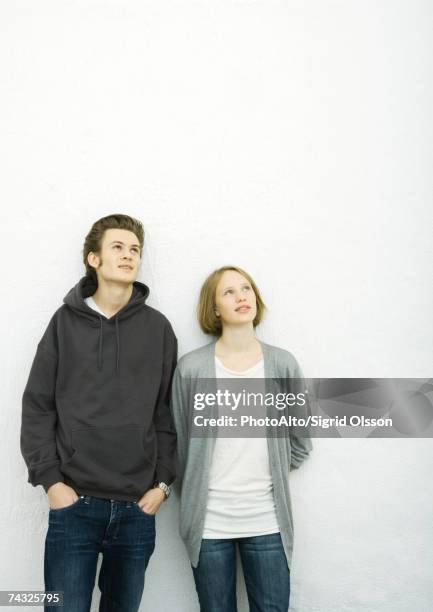 young couple leaning against wall, looking up - côte à côte photos et images de collection