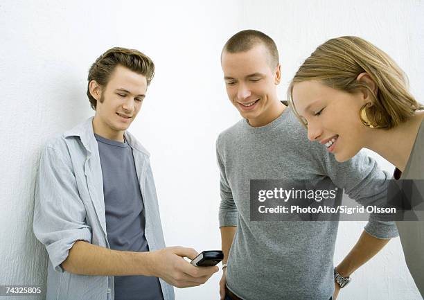 three young friends looking at cell phone, smiling - three quarter front view ストックフォトと画像