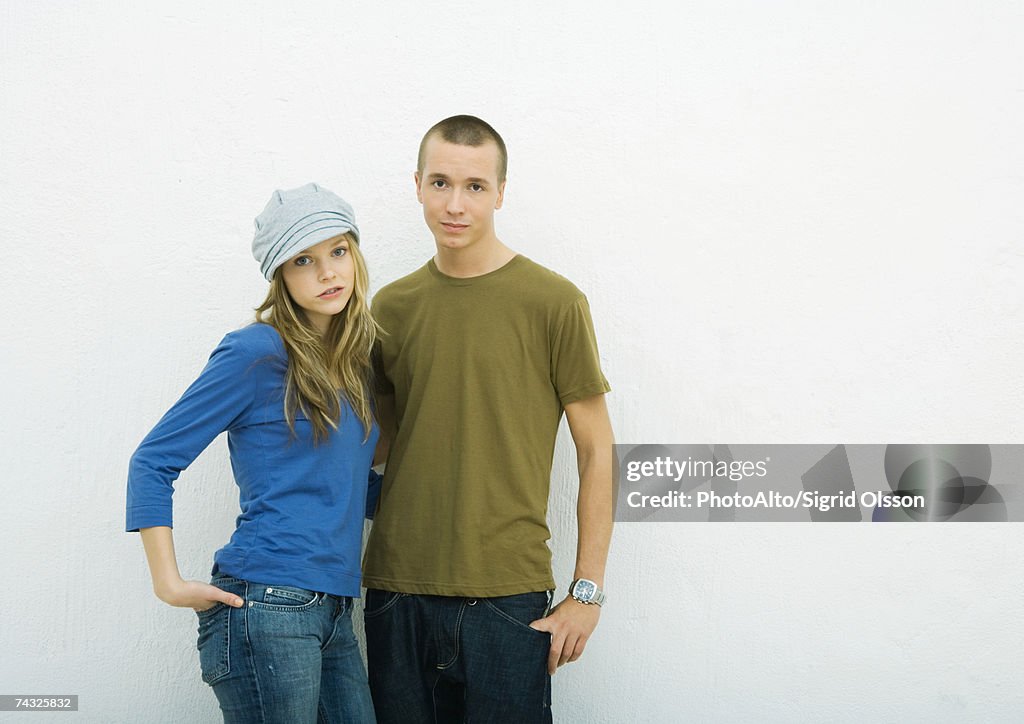 Young couple standing with hands in pockets, portrait, white background