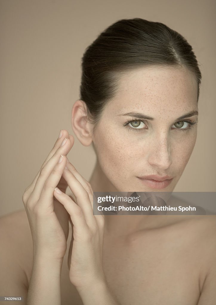 Woman with hands by face, looking at camera, portrait