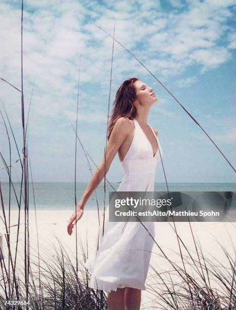 young woman in dress standing in dune grass with head back, facing wind - young woman white dress stock pictures, royalty-free photos & images