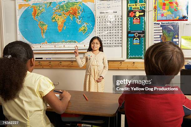 girl (8-9) demonstrating peace sign in front of classroom, other students watching - boy in briefs stock pictures, royalty-free photos & images