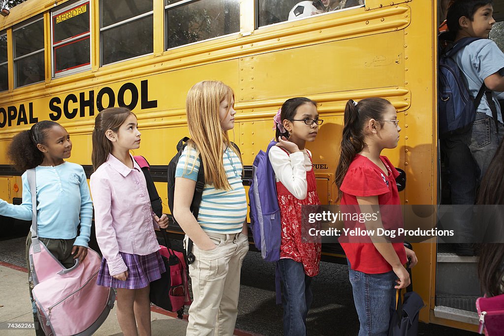 Children (8-11) lining up to board school bus, side view