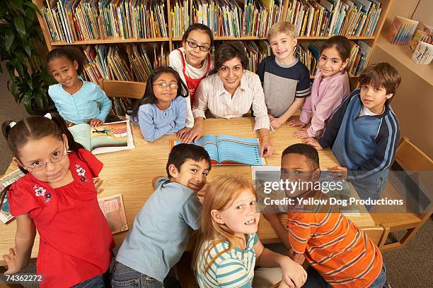 teacher sitting at table surrounded by children (9-10, 10-11) in school library, elevated view - circondare foto e immagini stock