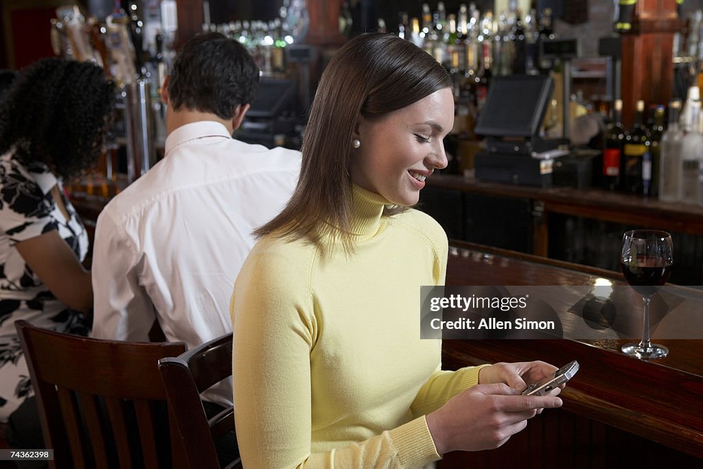 Woman text messaging using mobile phone at bar