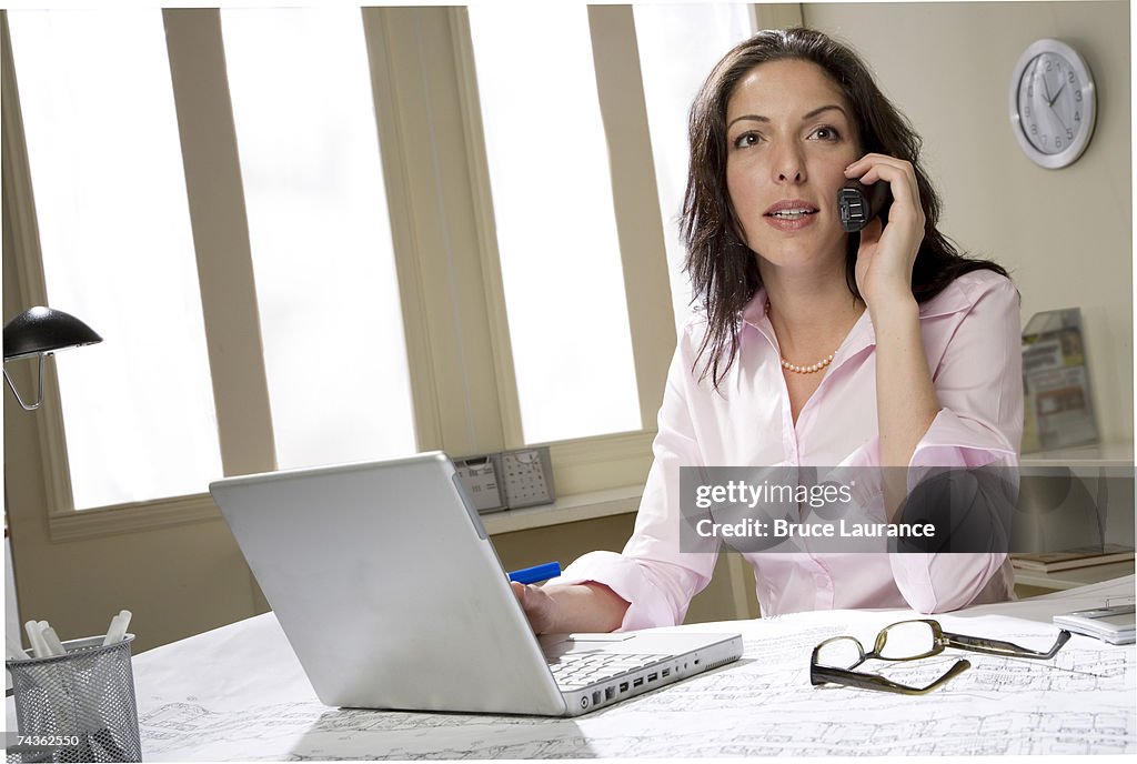 Young woman in office in front of laptop, talking on phone