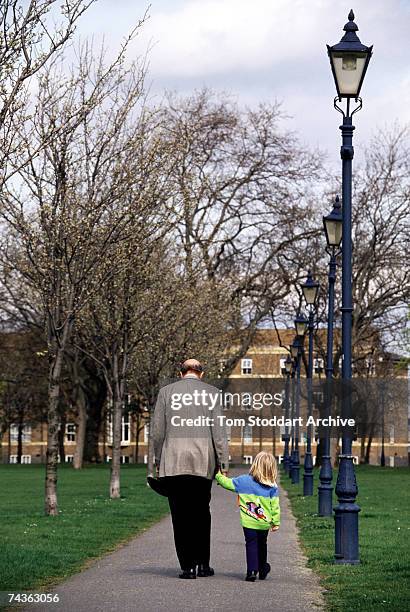 Grandfather holds the hand of his young granddaughter during a walk in a London park, April 1999.