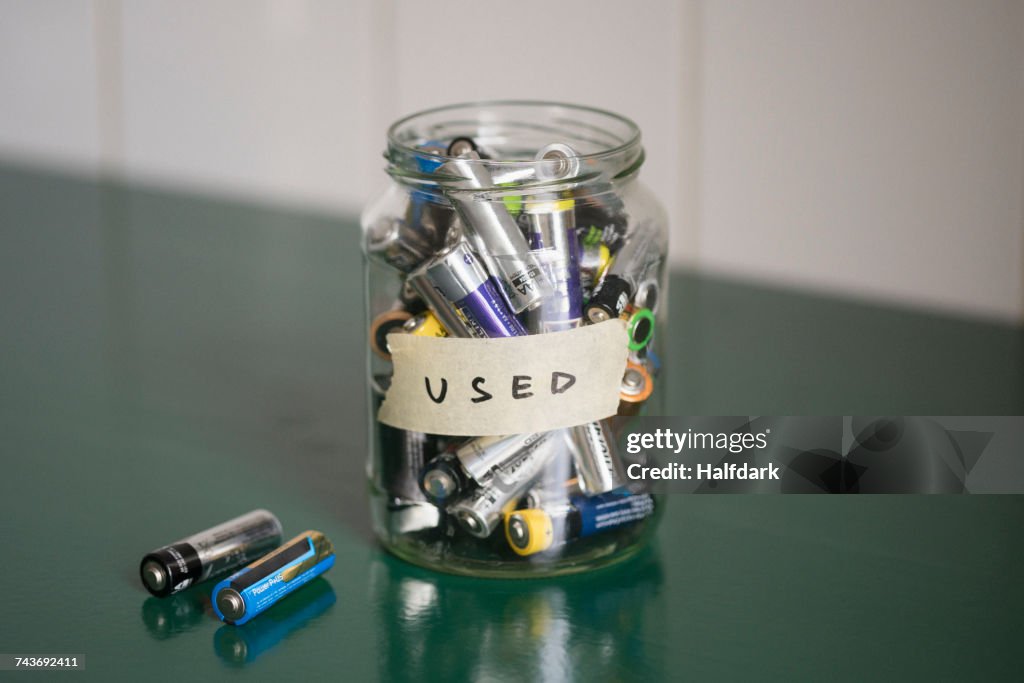 High angle view of batteries in glass jar with USED label on table