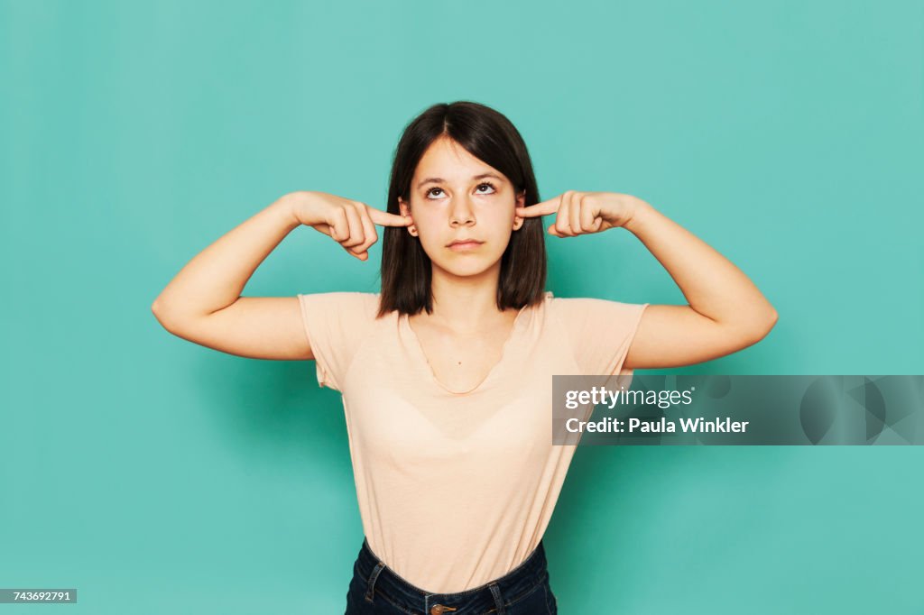 Girl looking up while covering ears against turquoise background