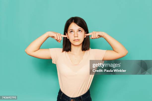 girl looking up while covering ears against turquoise background - handen over de oren stockfoto's en -beelden