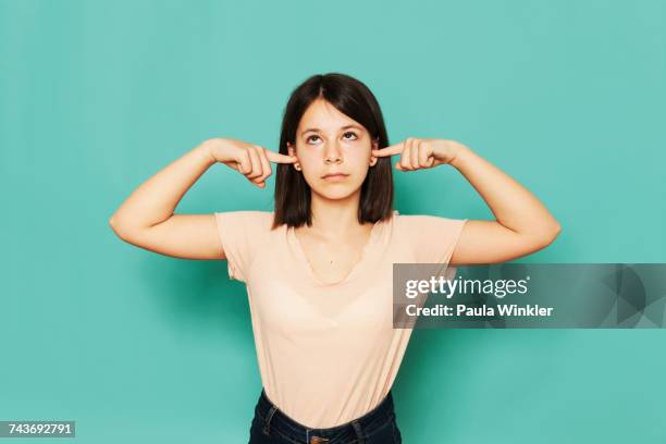 girl looking up while covering ears against turquoise background - not listening stock pictures, royalty-free photos & images