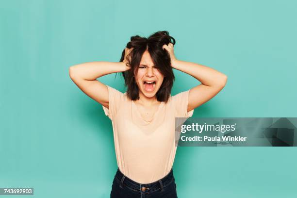 portrait of frustrated girl shouting with hands in hair against turquoise background - hand in hair stock pictures, royalty-free photos & images