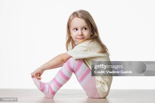 side view of cute girl sitting on floor against white background - small child sitting on floor stock-fotos und bilder