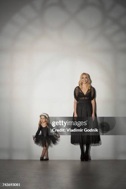 portrait of mother and daughter in black costume standing against wall at dance studio - ballett mädchen stock-fotos und bilder