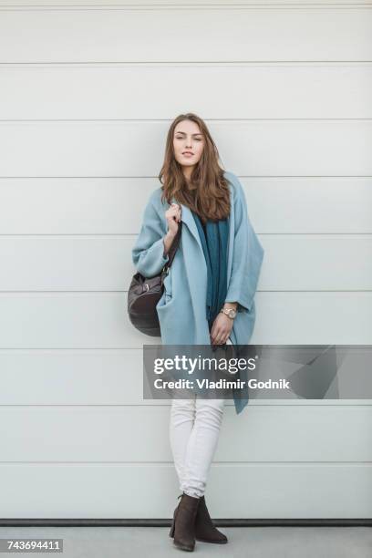 full length portrait of beautiful woman carrying backpack standing by wall - woman standing full length stock pictures, royalty-free photos & images