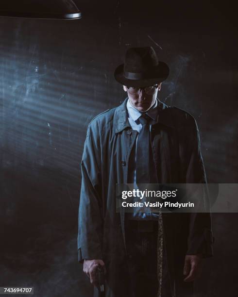 young man standing with gun against black wall - detective trench coat fotografías e imágenes de stock