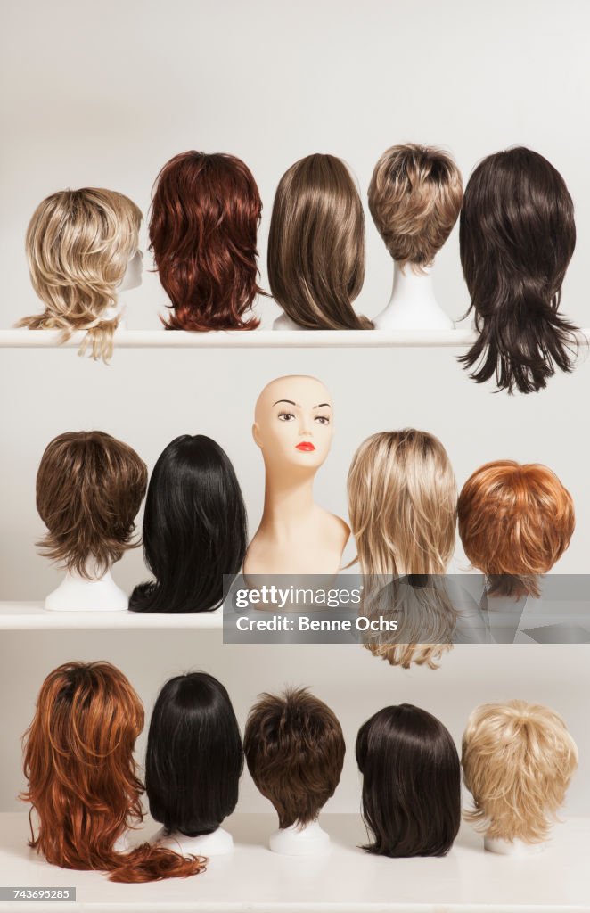 Mannequin head amidst various wigs on shelves against white background