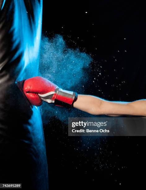cropped image of man hitting punching bag against black background - prügelei stock-fotos und bilder