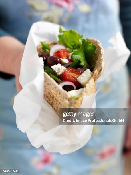 a woman holding a pita bread filled with greek salad - fetta stockfoto's en -beelden