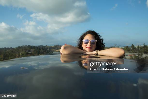 smiling mid adult woman leaning on car roof against sky, los angeles, california, usa - car roof stock pictures, royalty-free photos & images