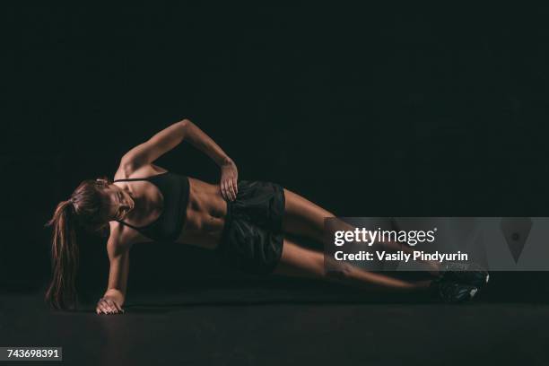 full length of determined woman doing side plank exercise against black background - side plank pose stock pictures, royalty-free photos & images